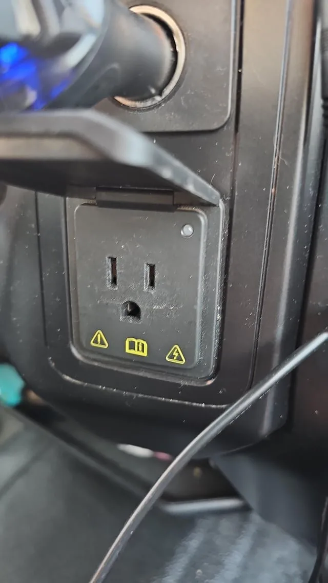 A power tool cord being plugged into a truck bed 120-volt power outlet.