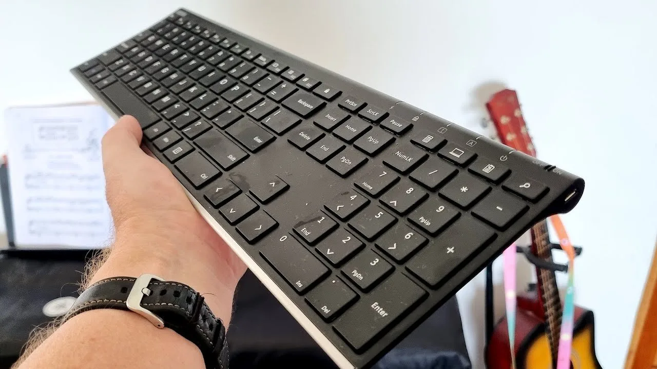 A wireless keyboard receiver plugged into a laptop port on a wooden desk.