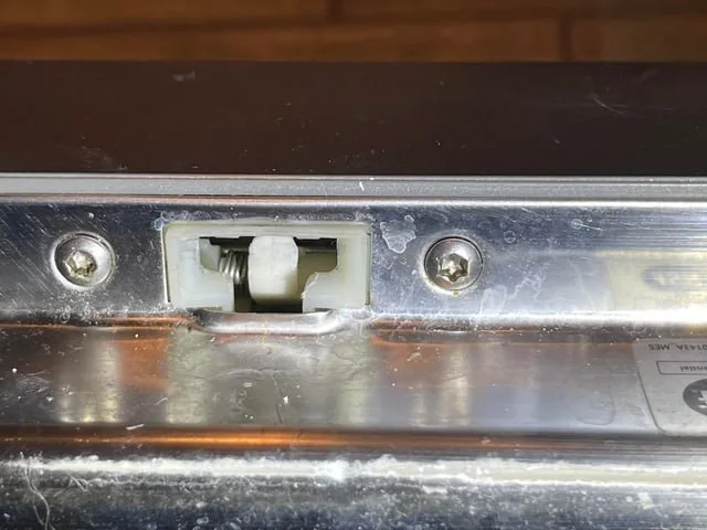 Hands pressing firmly against a dishwasher door to release a stuck latch.