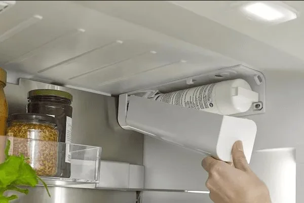 A person holding a replacement water filter cartridge for a refrigerator repair.