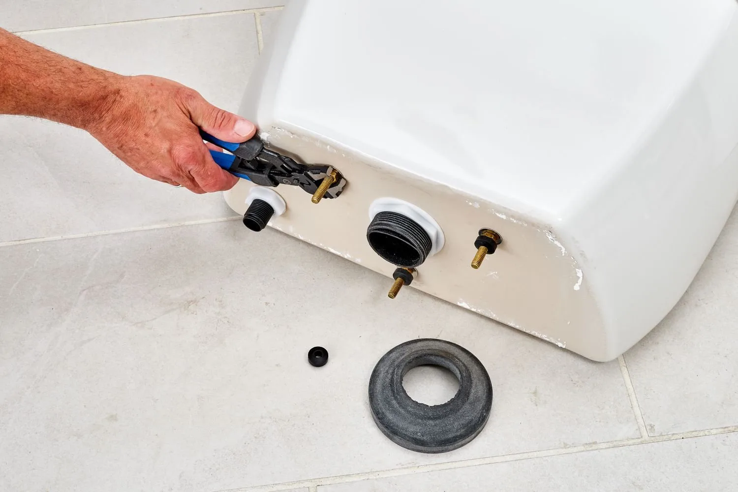 Applying plumber's putty to a toilet tank bolt washer for a seal.